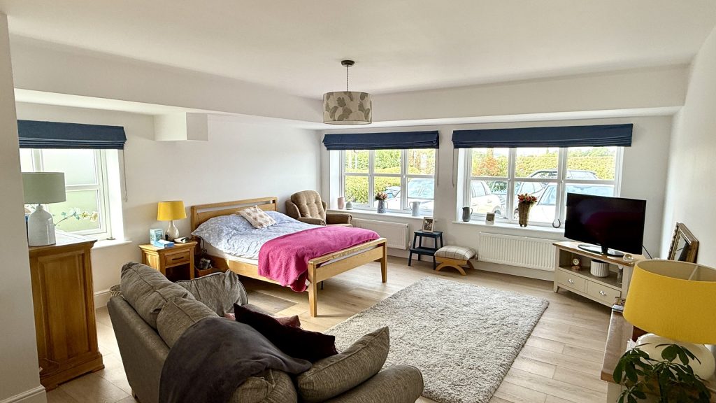 Cozy Bright Bedroom Oasis with Stylish Decor Spacious bedroom with natural light, queen bed, stylish decor, and cozy seating area.